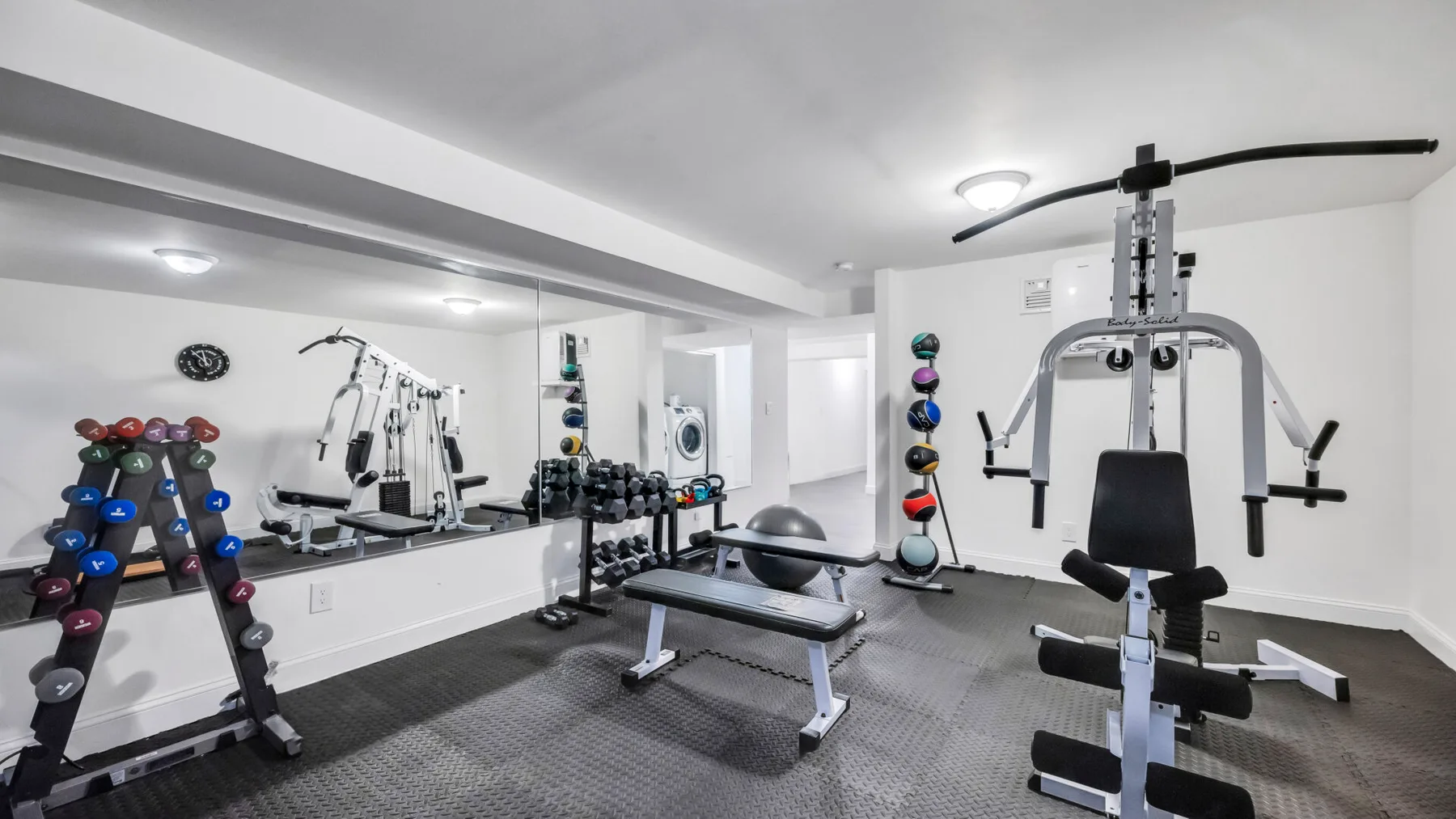 A home gym with weight machines, dumbbells, and a workout bench.