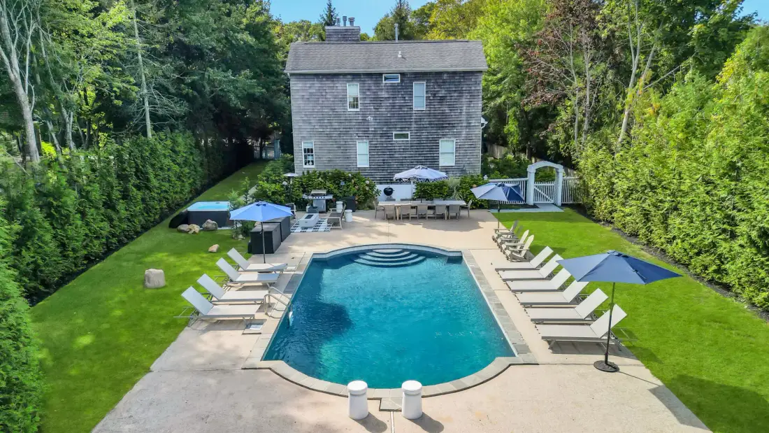 An outdoor swimming pool is surrounded by lounge chairs and green lawn.
