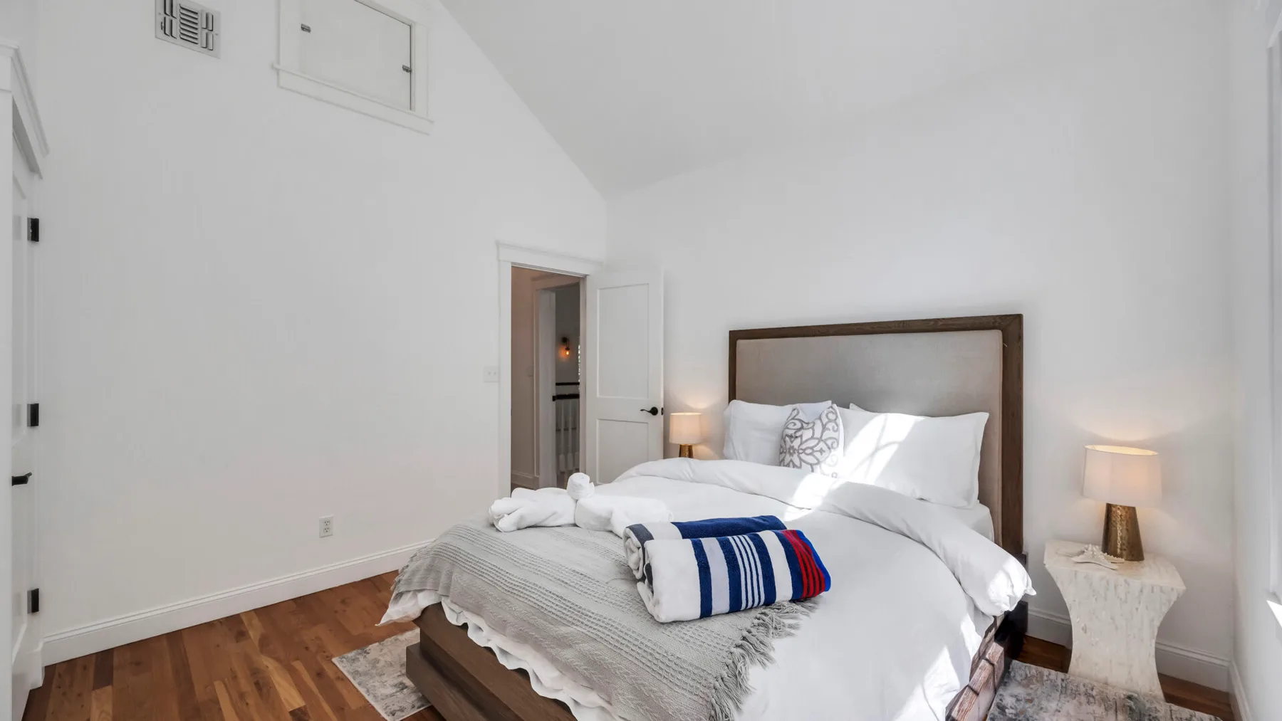 A bright bedroom with a bed dressed in white linens and a striped blanket.