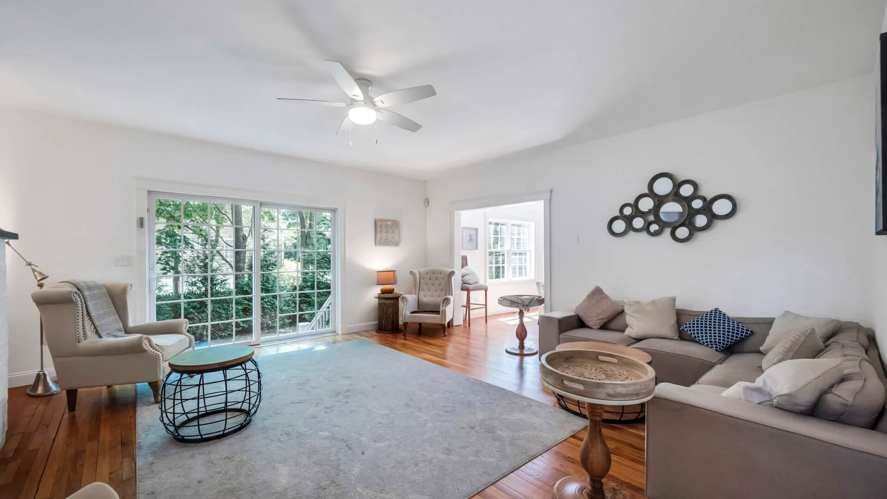 A bright living room with a large rug, seating, and windows overlooking greenery.