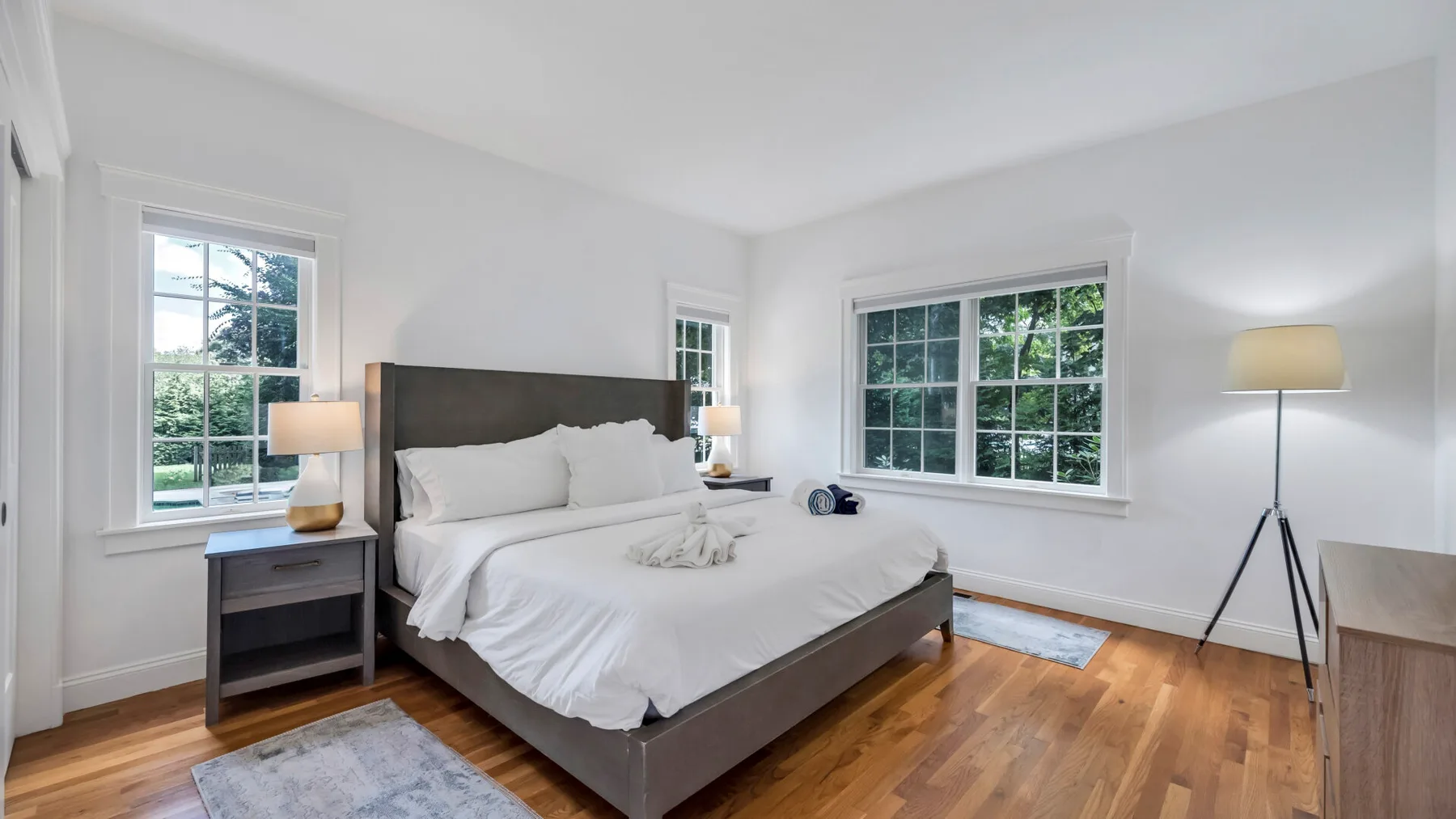 A bright bedroom with a bed, bedside tables, and large windows.