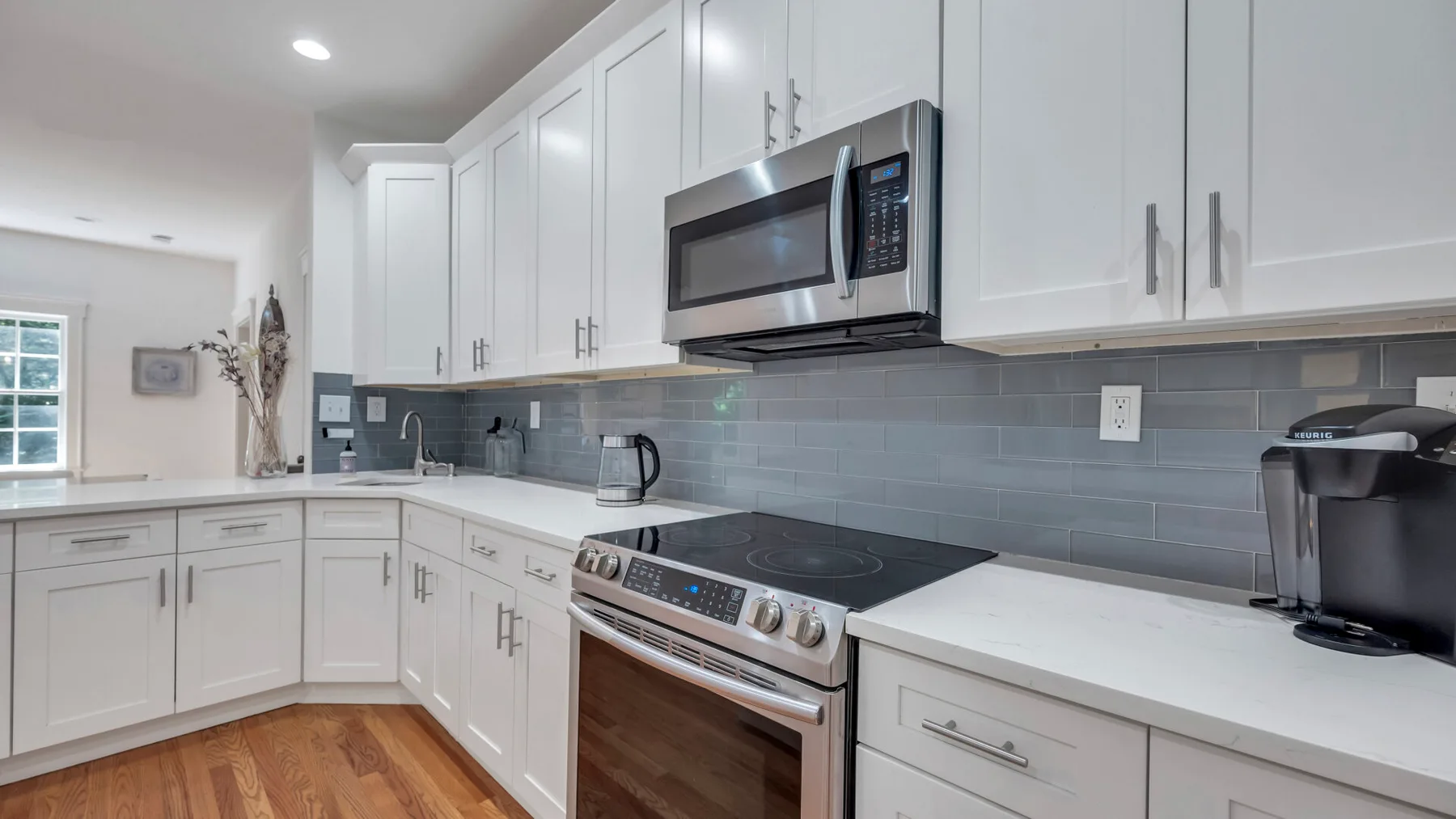 A bright kitchen with white cabinets, stainless steel appliances, and a gray tile backsplash.
