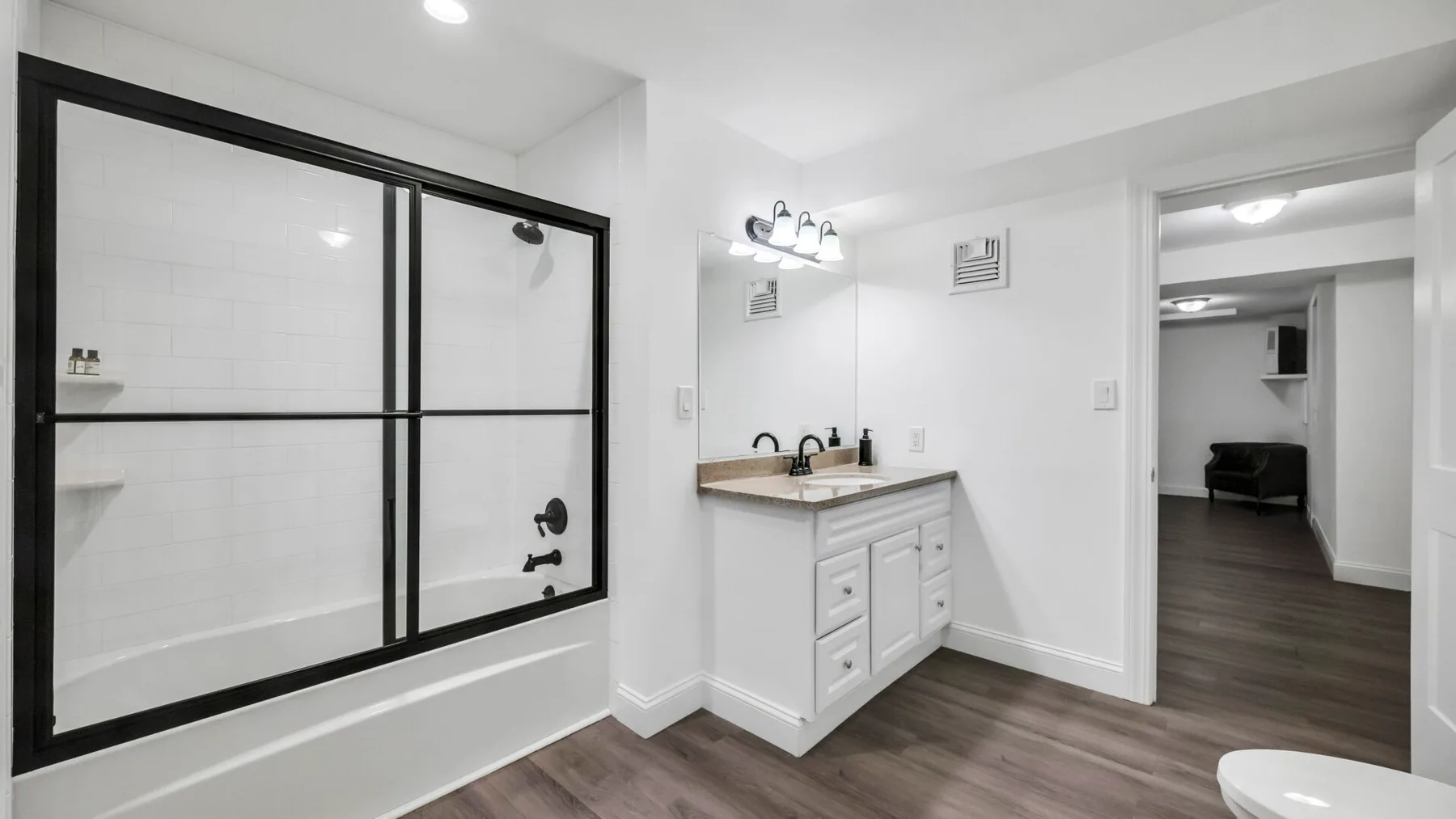 A bright bathroom with a glass shower, vanity, and an open doorway.