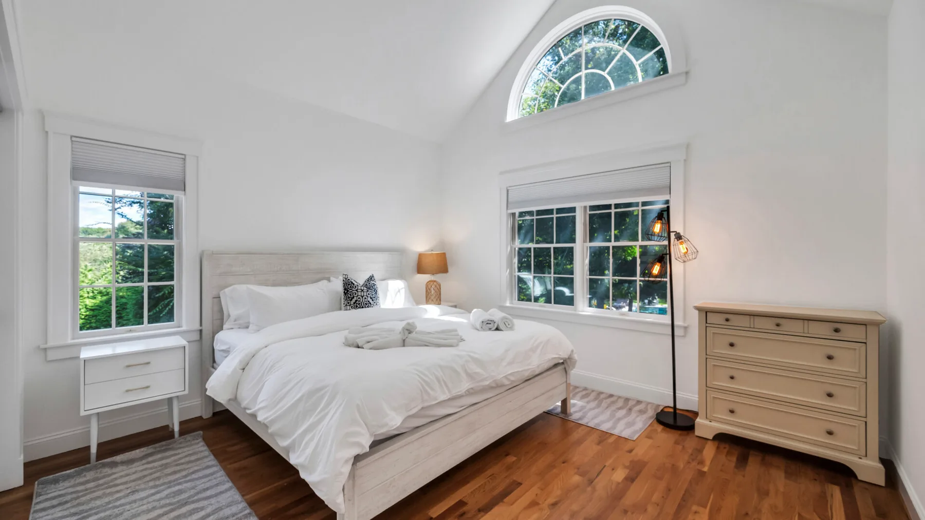 A bright bedroom with a bed, large windows, and a wooden dresser.