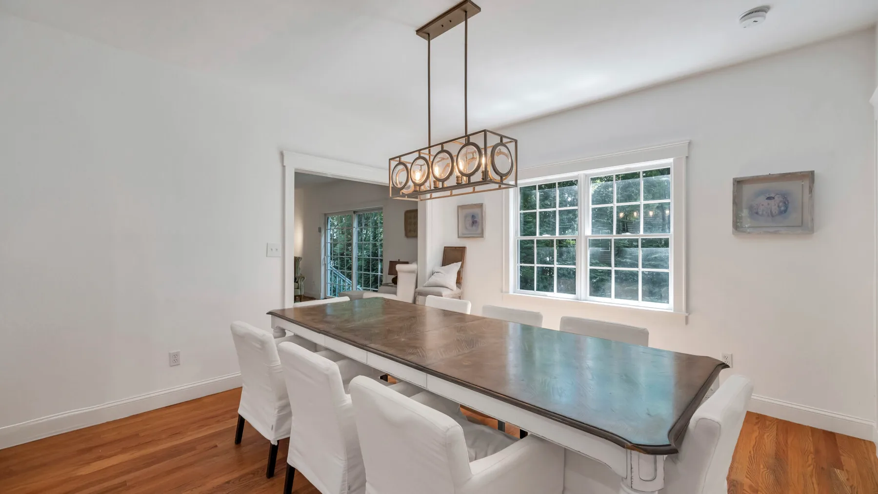 A dining area with a long table and white seating beneath a hanging light.