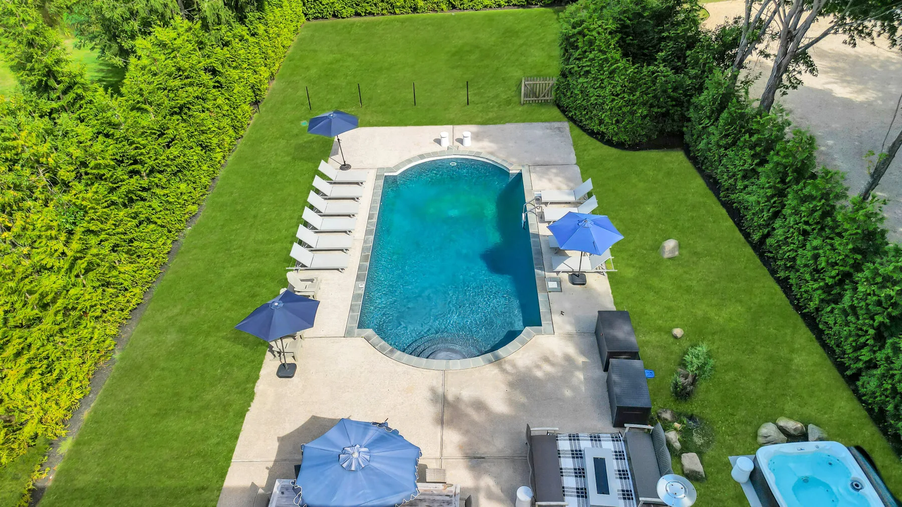 An outdoor swimming pool is set in a grassy garden surrounded by hedges.