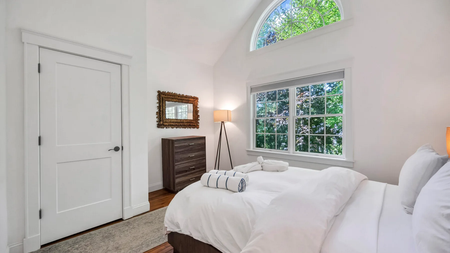 A bright bedroom with white bedding and large windows.