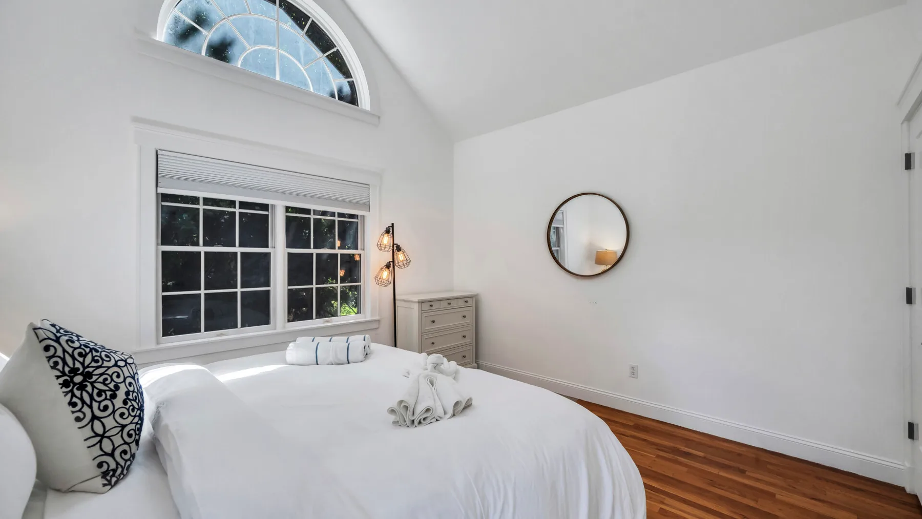 A bright bedroom with a bed beneath a large window and arched upper window.