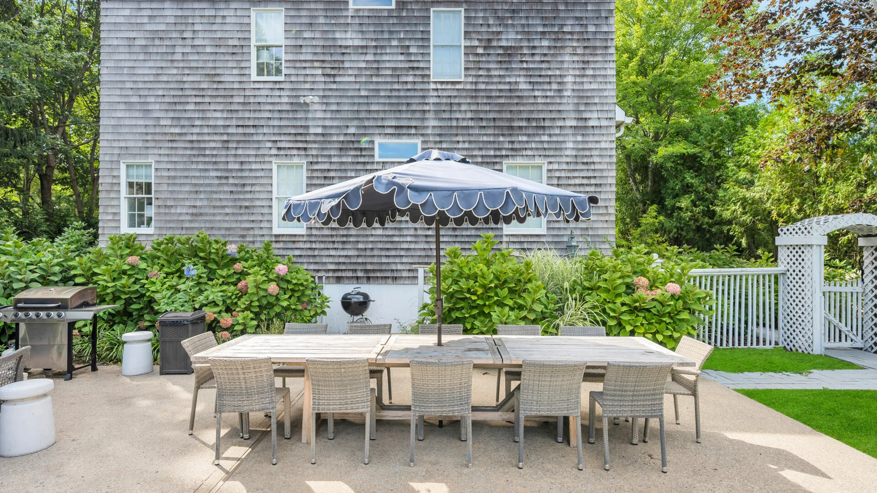 An outdoor dining patio with a long table beneath a large umbrella.