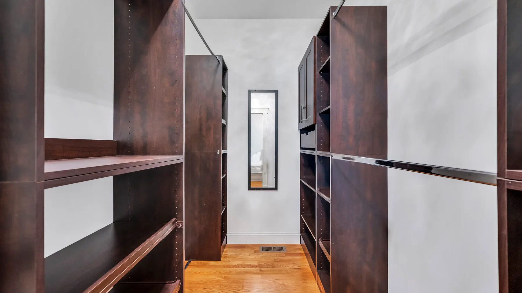 A walk-in closet with dark built-in shelving and a wooden floor.