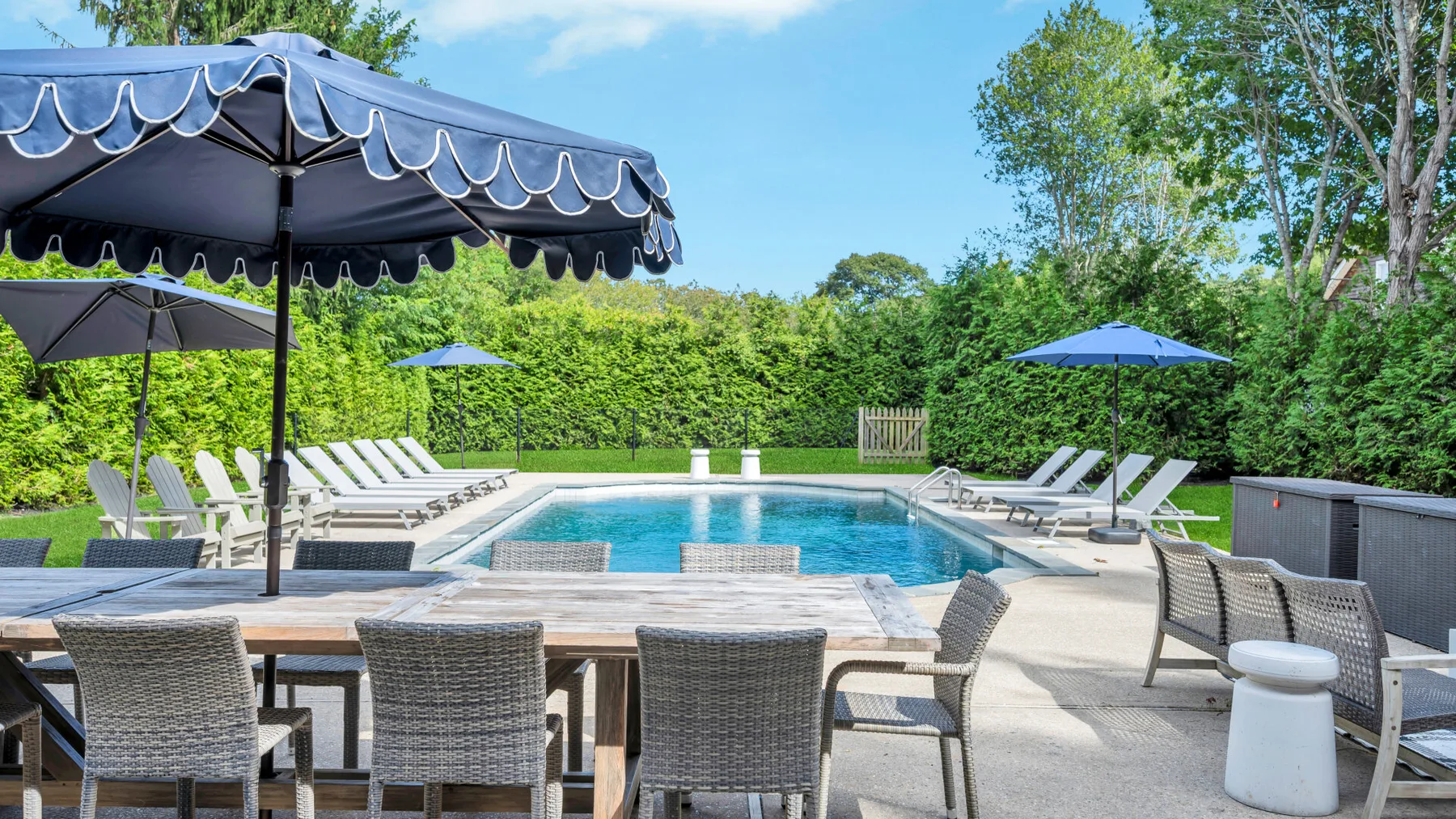 A swimming pool is surrounded by outdoor seating and shade umbrellas.