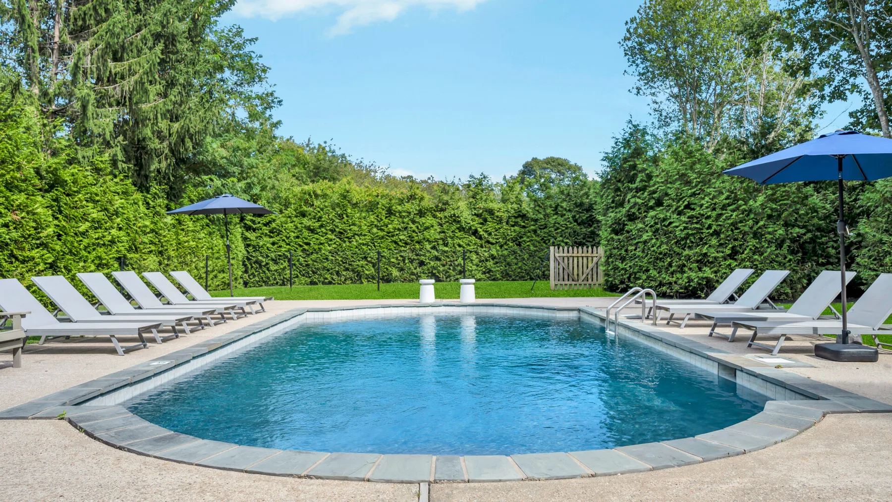 An outdoor swimming pool is surrounded by lounge seating and green hedges.