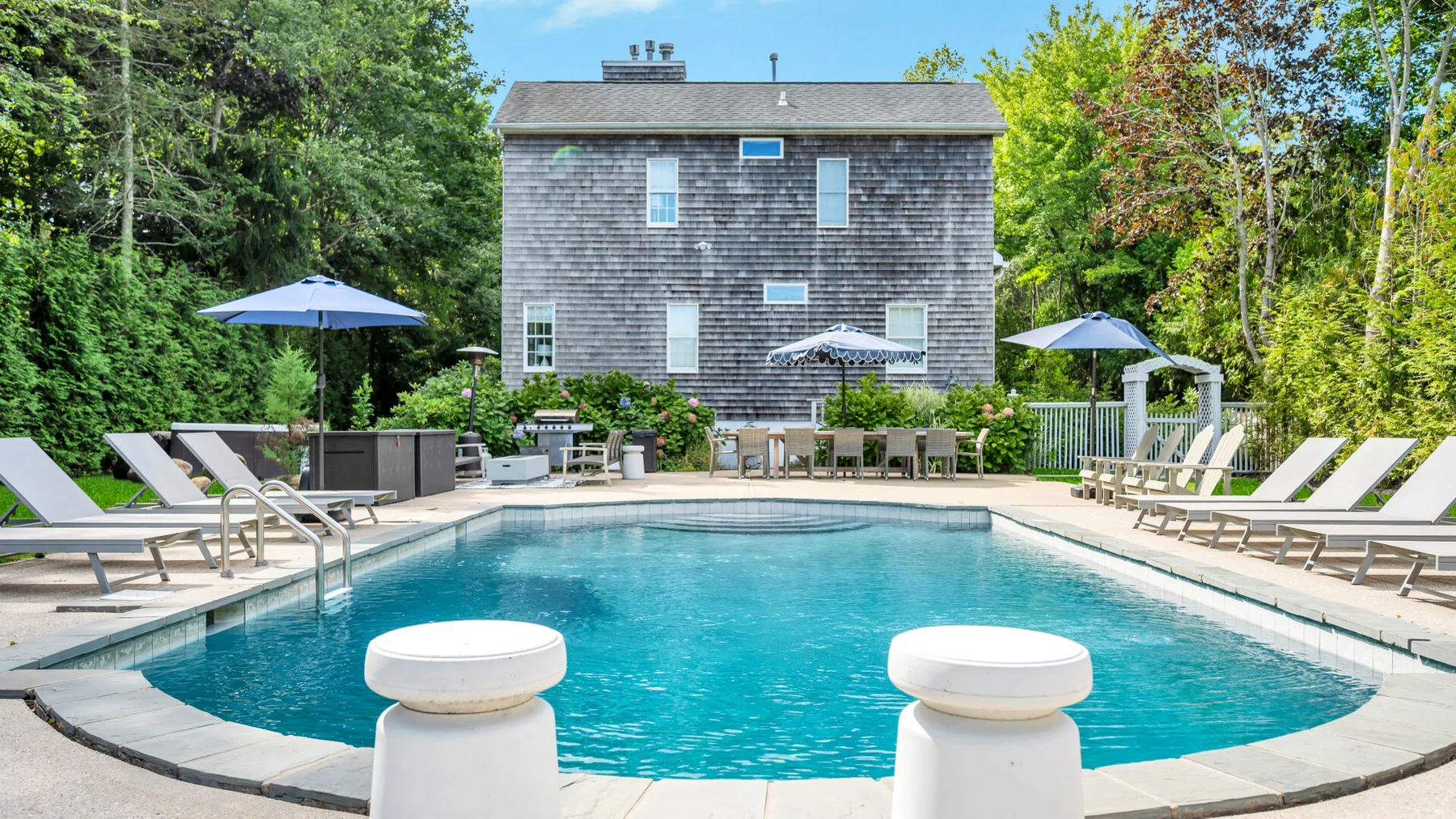 An outdoor swimming pool sits beside a shingled building, with lounge seating around it.