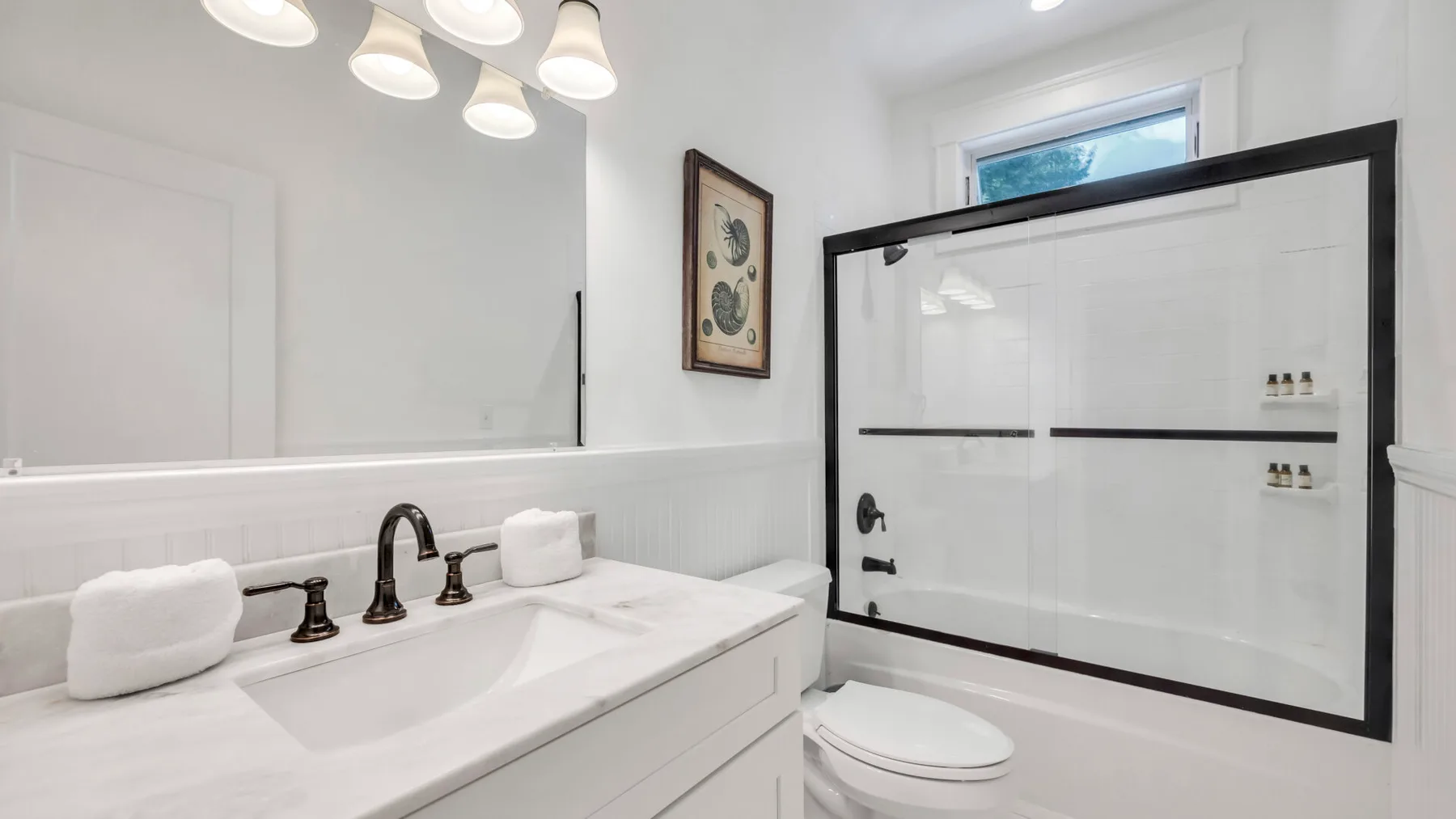 A bright bathroom with a wide vanity and a bathtub behind a glass screen.