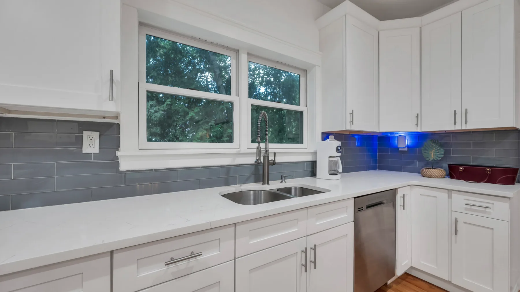 A bright kitchen with white cabinetry, a sink, and a window overlooking trees.