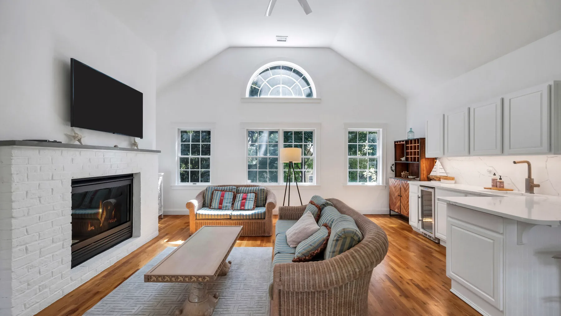 A bright open-plan living room and kitchen with seating, a fireplace, and large windows.
