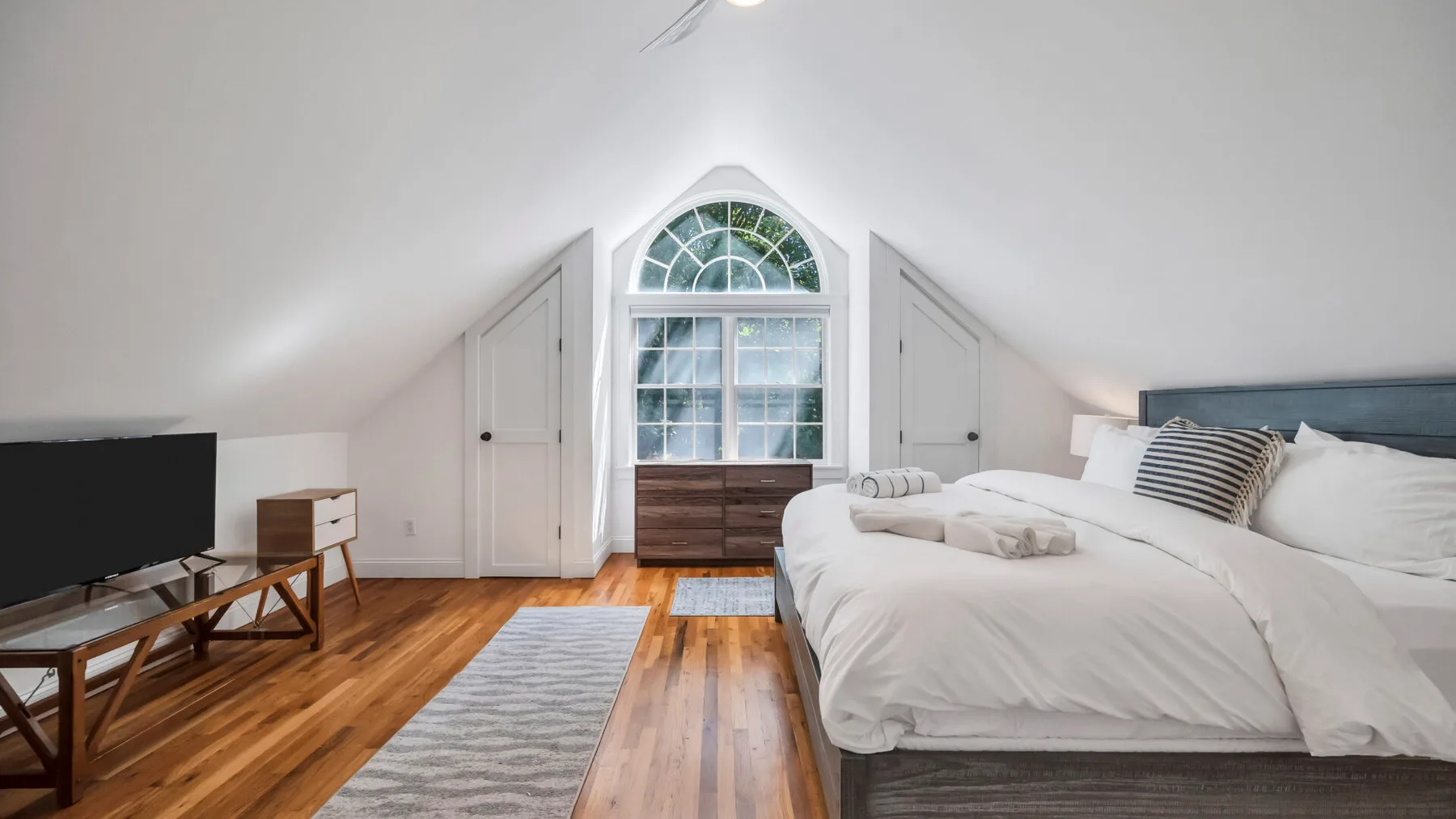 A bright attic bedroom with a large bed beneath an arched window.