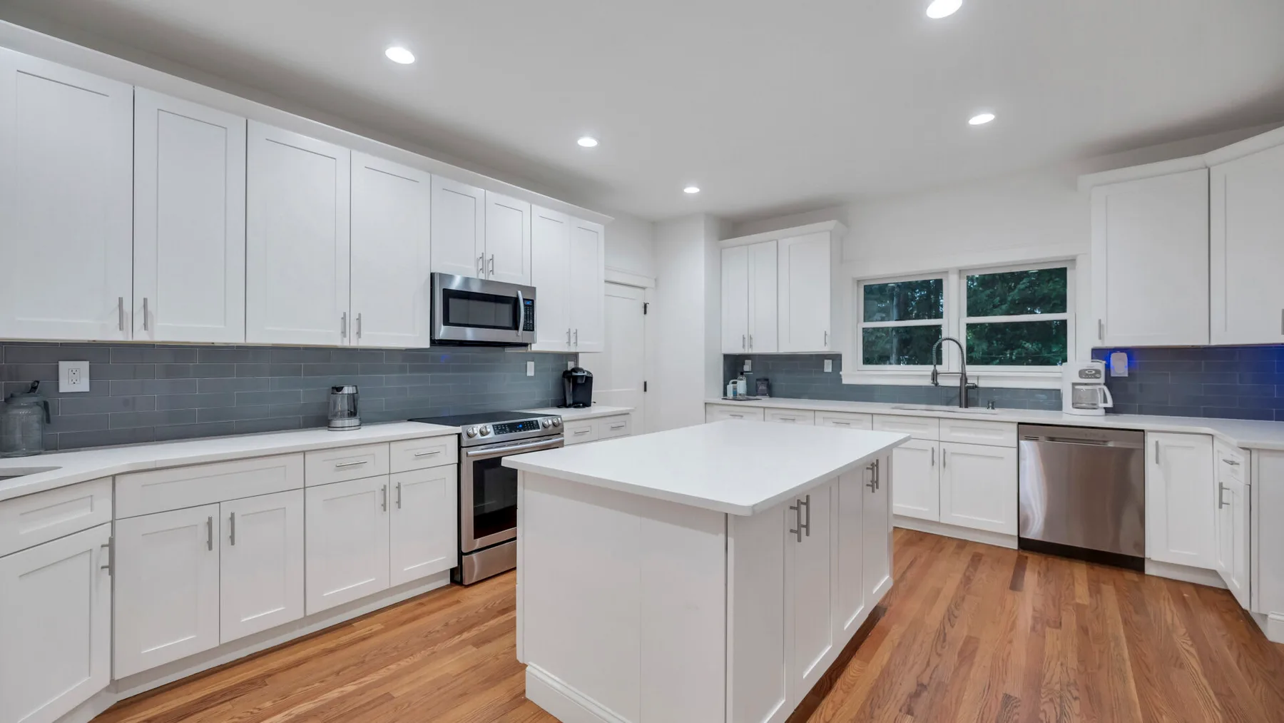 A bright kitchen with white cabinetry, a central island, and wood flooring.