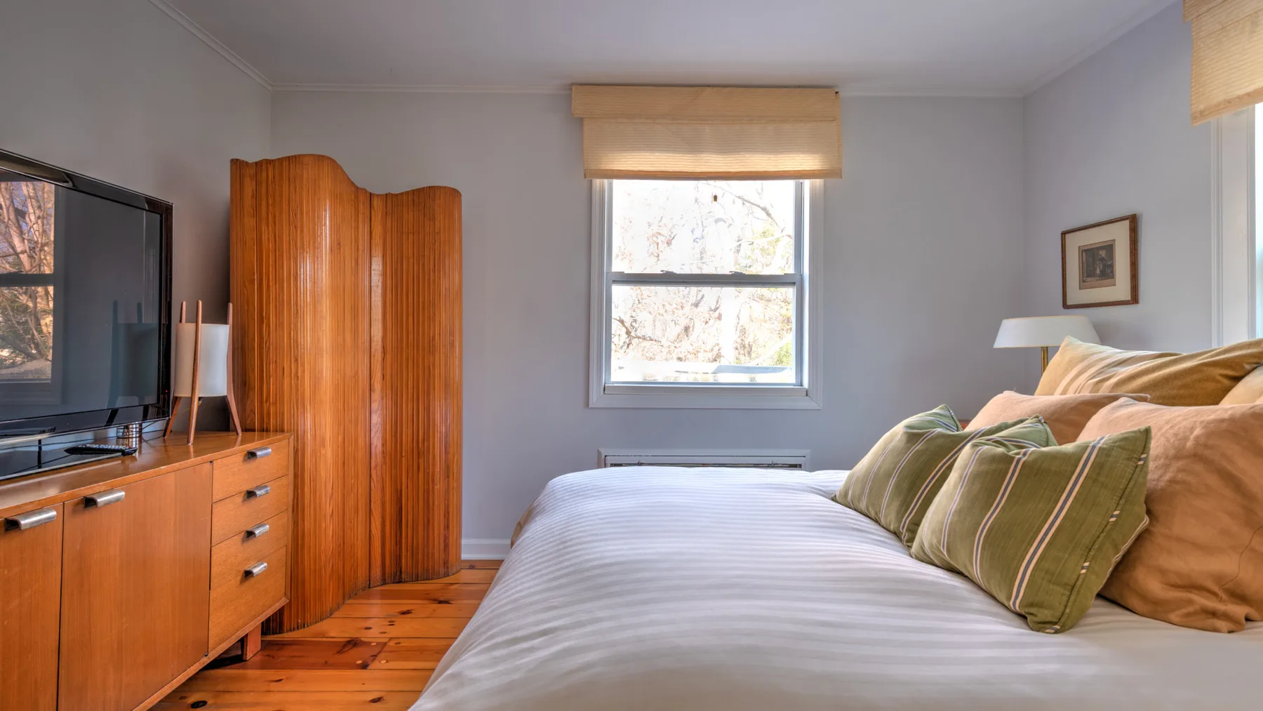 Un dormitorio con una cama, cojines verdes y muebles de madera.