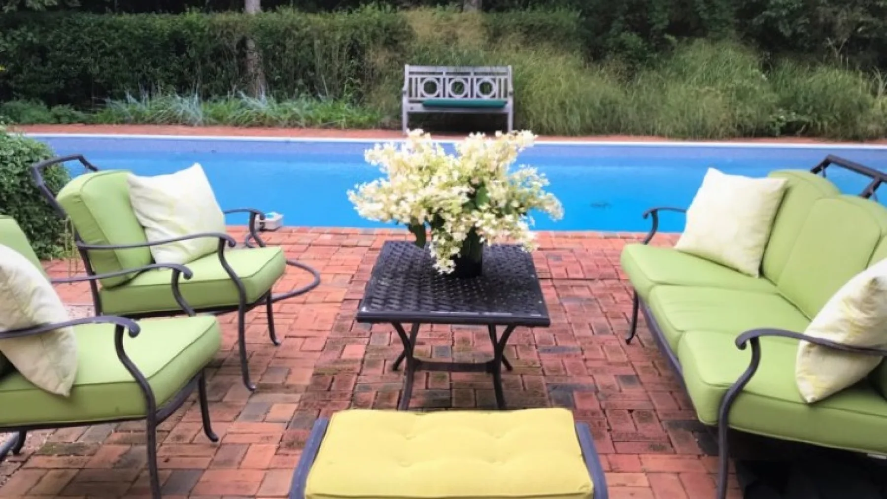 Una zona de estar junto a la piscina con cojines verdes y flores sobre una mesa.