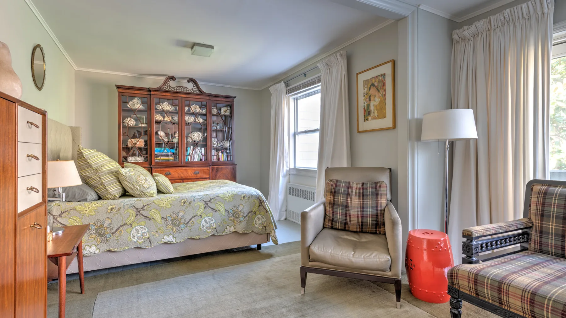 Un dormitorio con una cama, un armario vitrina y un sillón junto a la ventana.