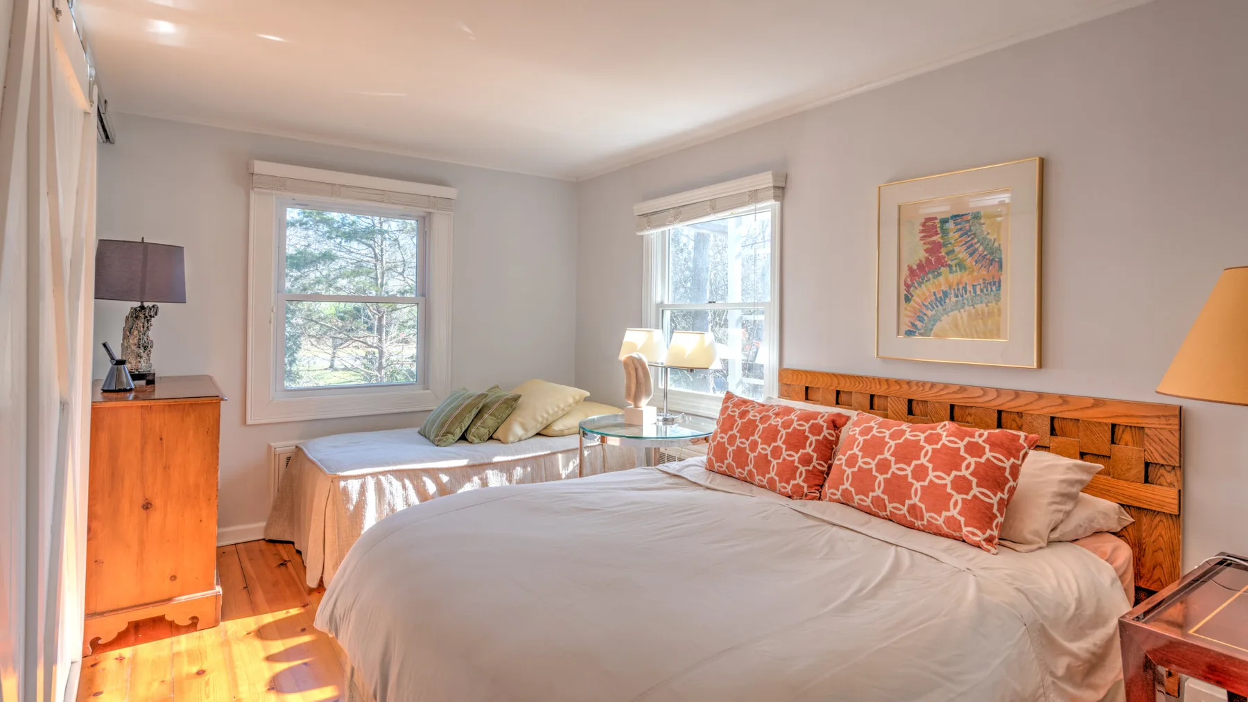 Un dormitorio luminoso con una cama, cojines estampados y ventanas.