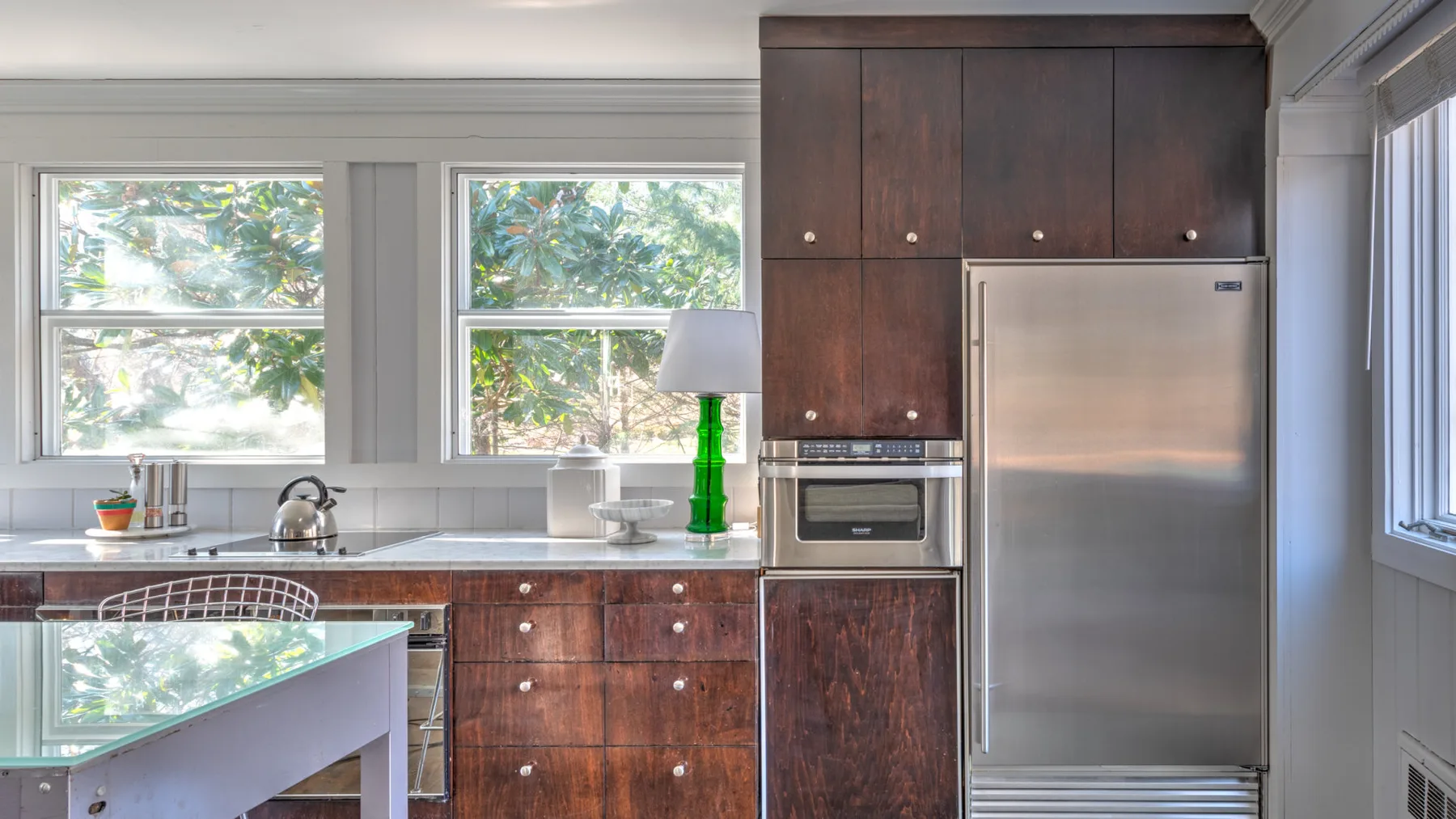 Una cocina con gabinetes de madera oscura, un refrigerador y ventanas amplias.