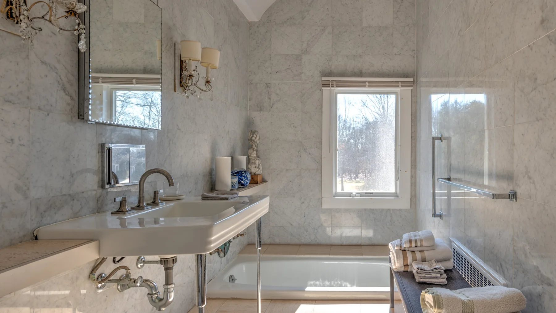 Baño revestido de mármol con bañera, lavabo y dos ventanas.