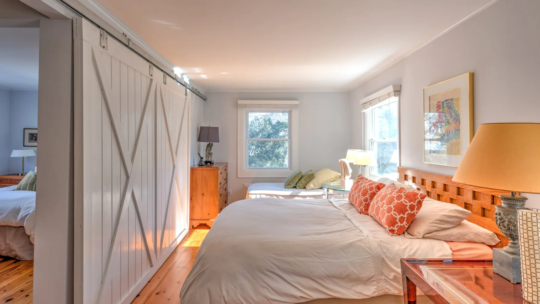 Un dormitorio con una cama grande, ropa de cama clara y ventanas con vistas a la vegetación.