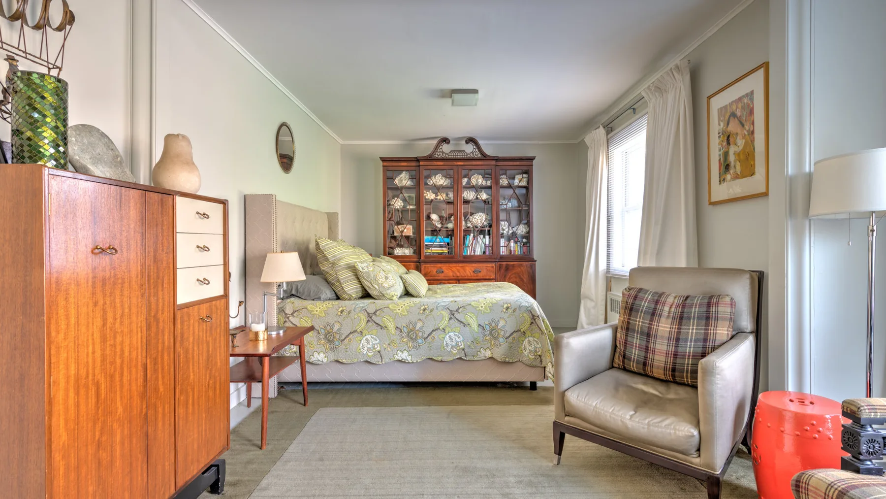 Un dormitorio con una cama, un armario de madera y un sillón acolchado.