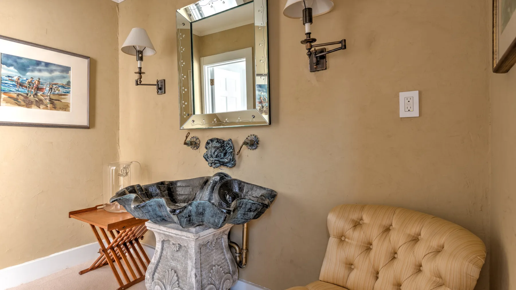 Un tocador de baño con lavabo decorativo, espejo y asiento tapizado.