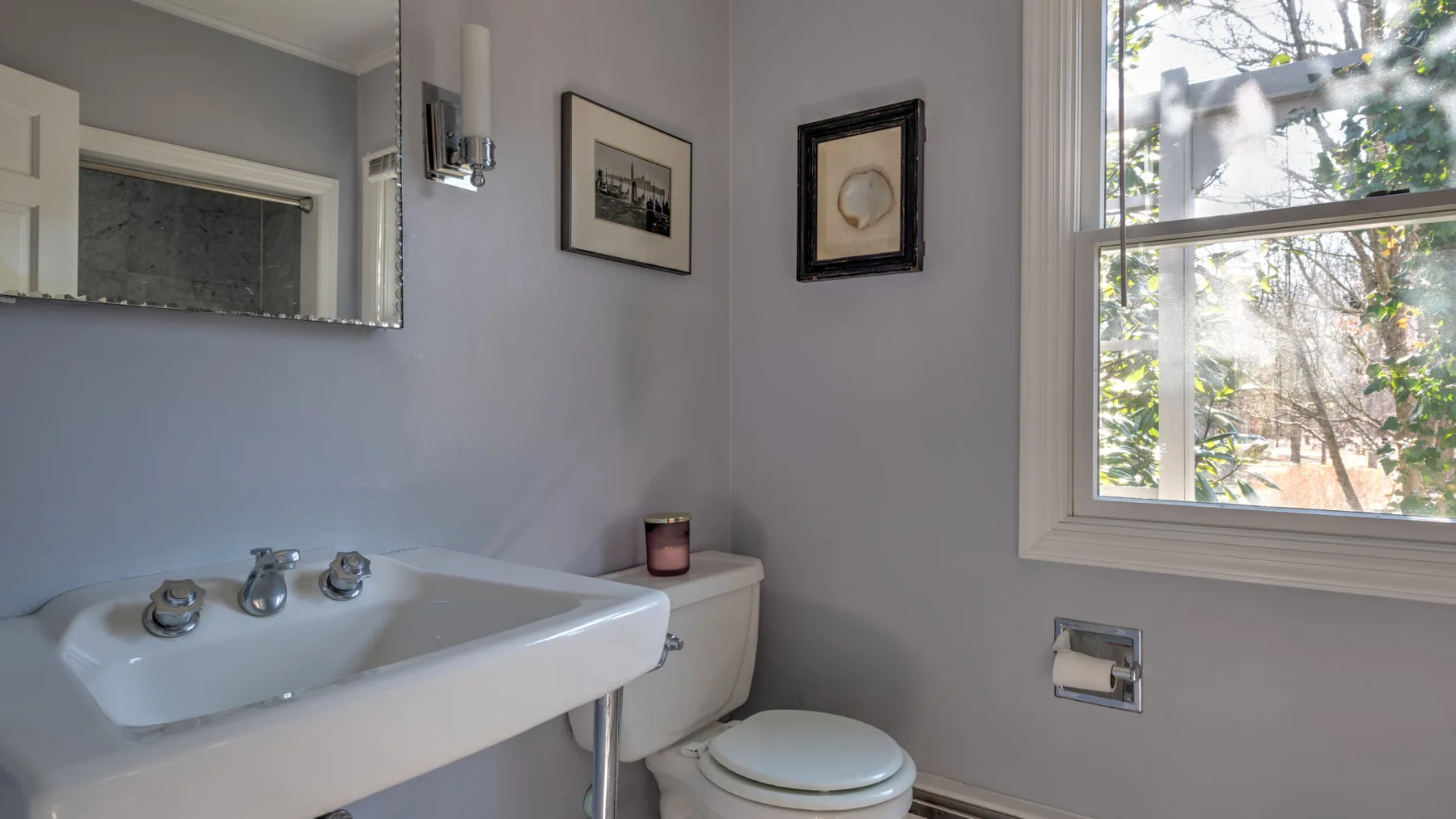 Un baño con lavabo, inodoro y una ventana con vista a los árboles.