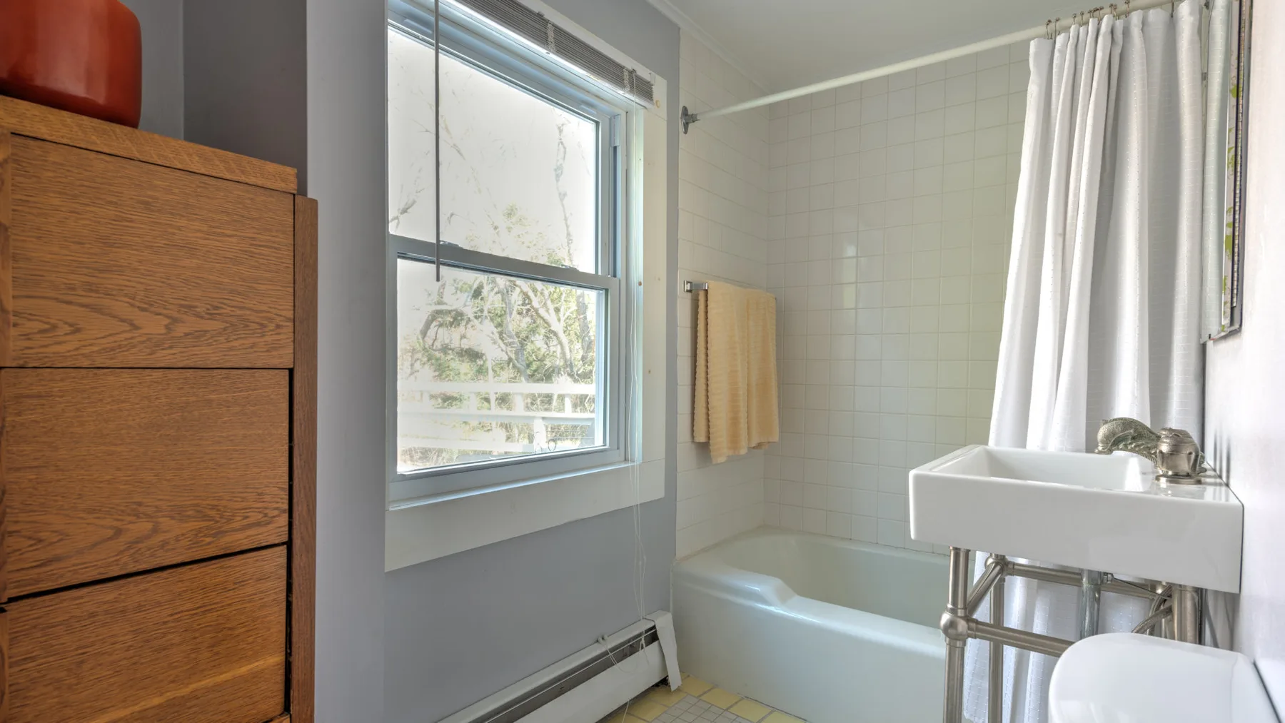 Un baño luminoso con bañera, cortina de ducha y lavabo con pedestal.