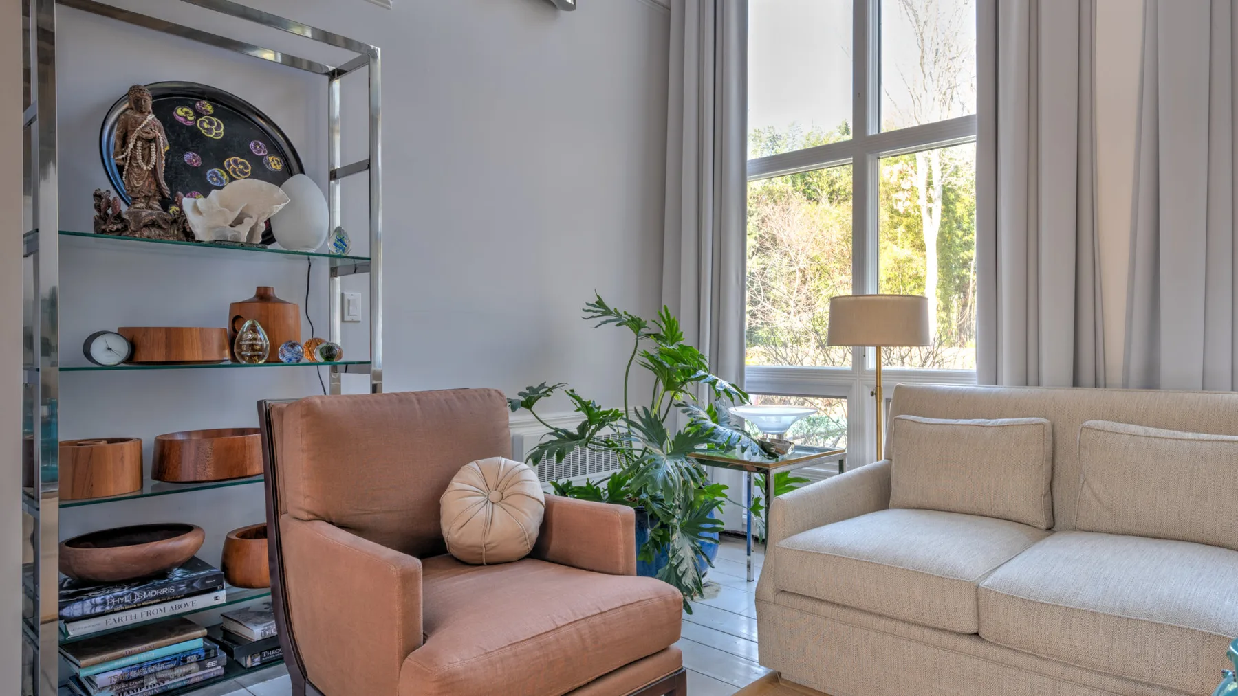 Una sala luminosa tiene asientos junto a una ventana grande y una estantería decorativa.