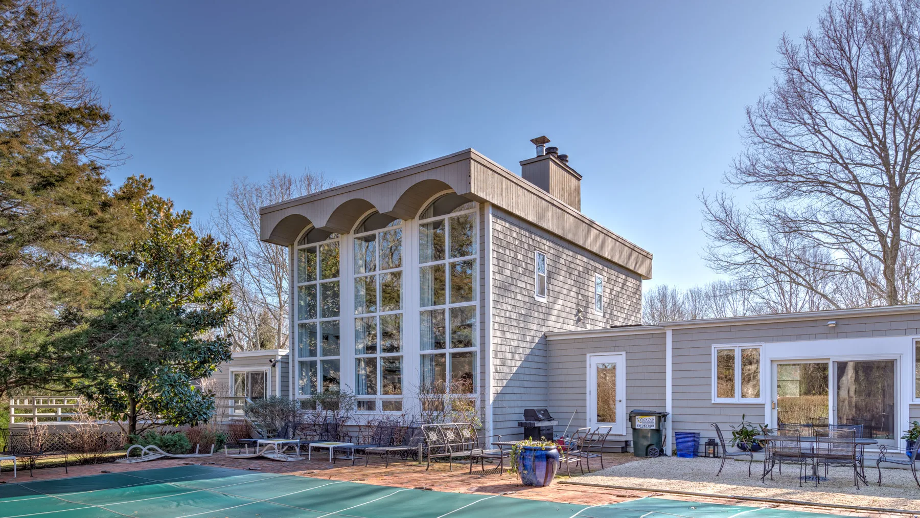 Una casa moderna con una alta fachada de vidrio da a una piscina y un patio.