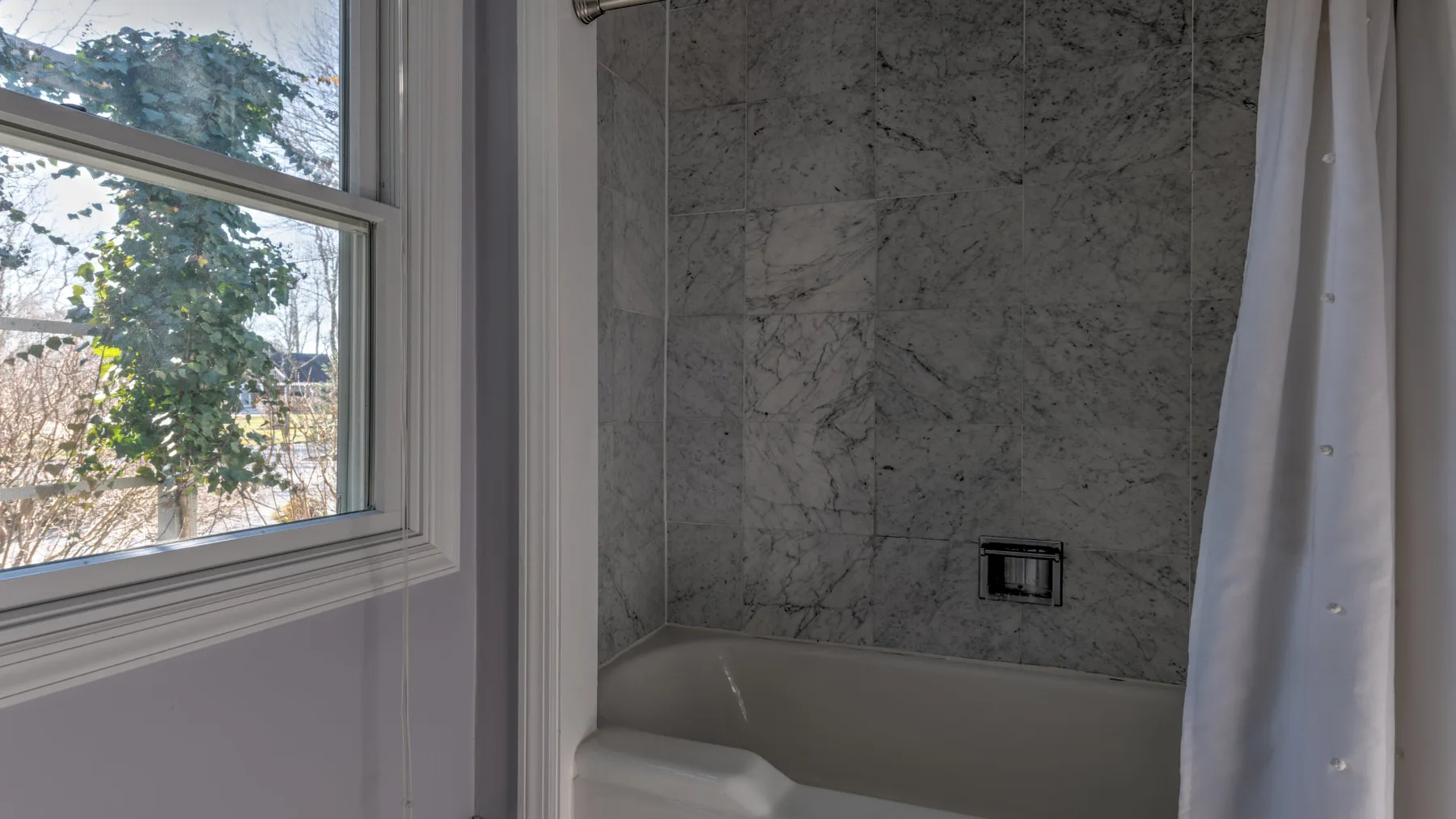 Un baño con bañera, pared de aspecto marmóreo y ventana.