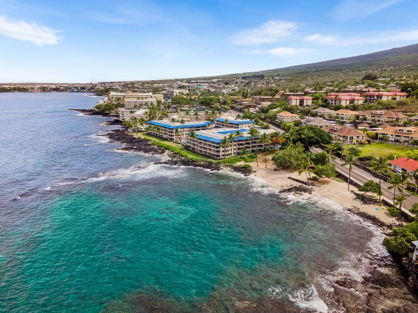 Vista aérea de la costa con agua turquesa, un litoral rocoso y edificios junto a la playa.