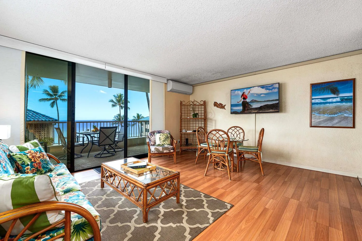 Una sala de estar y comedor da a un balcón con palmeras y vistas al mar.