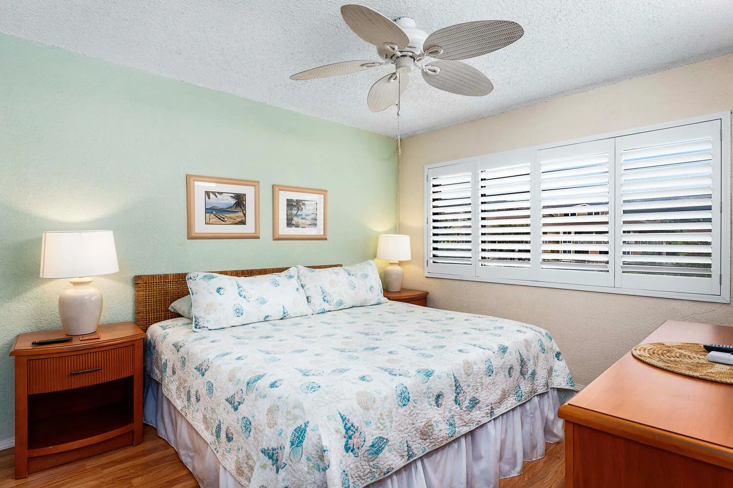 Un dormitorio con una cama bajo un ventilador de techo y ventanas con persianas.