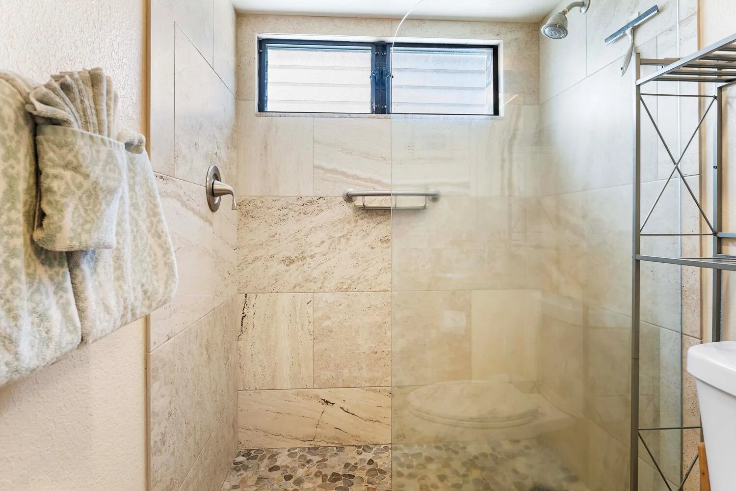 Un baño alicatado tiene una ducha de vidrio y una ventana alta pequeña.