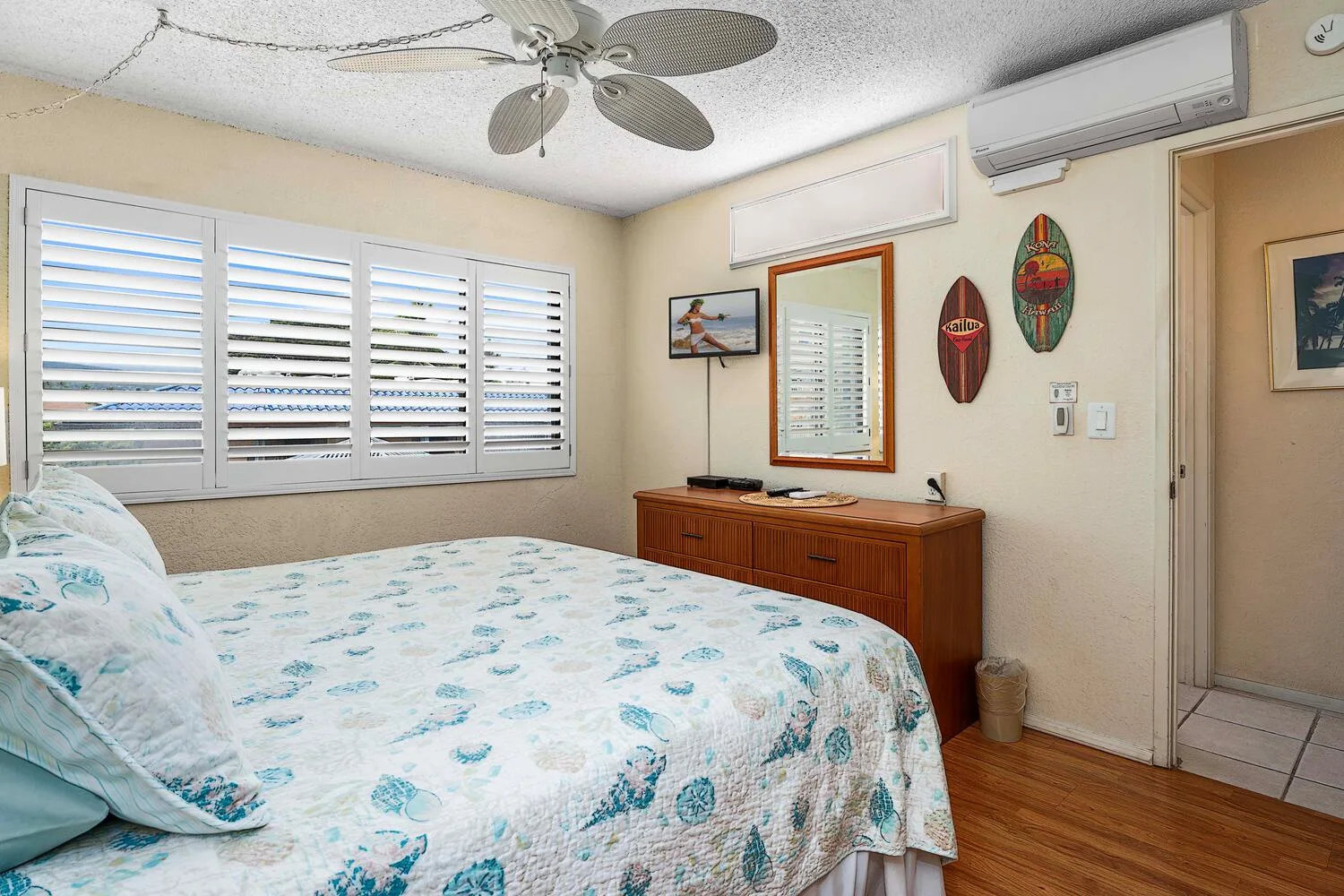 Un dormitorio con una cama bajo ventanas con contraventanas y una cómoda de madera.