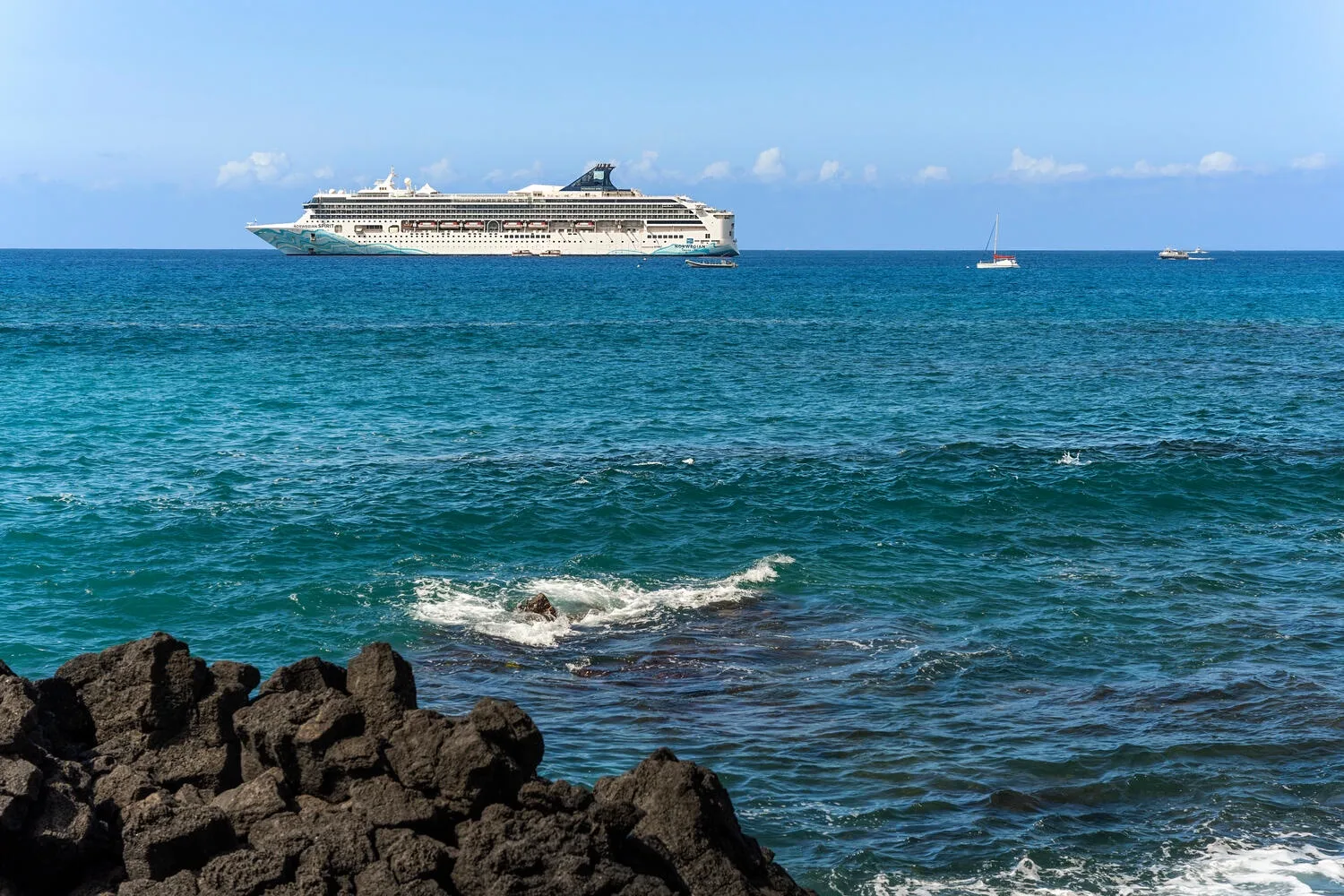 Un crucero navega por el mar, más allá de las olas que rompen contra una costa rocosa.