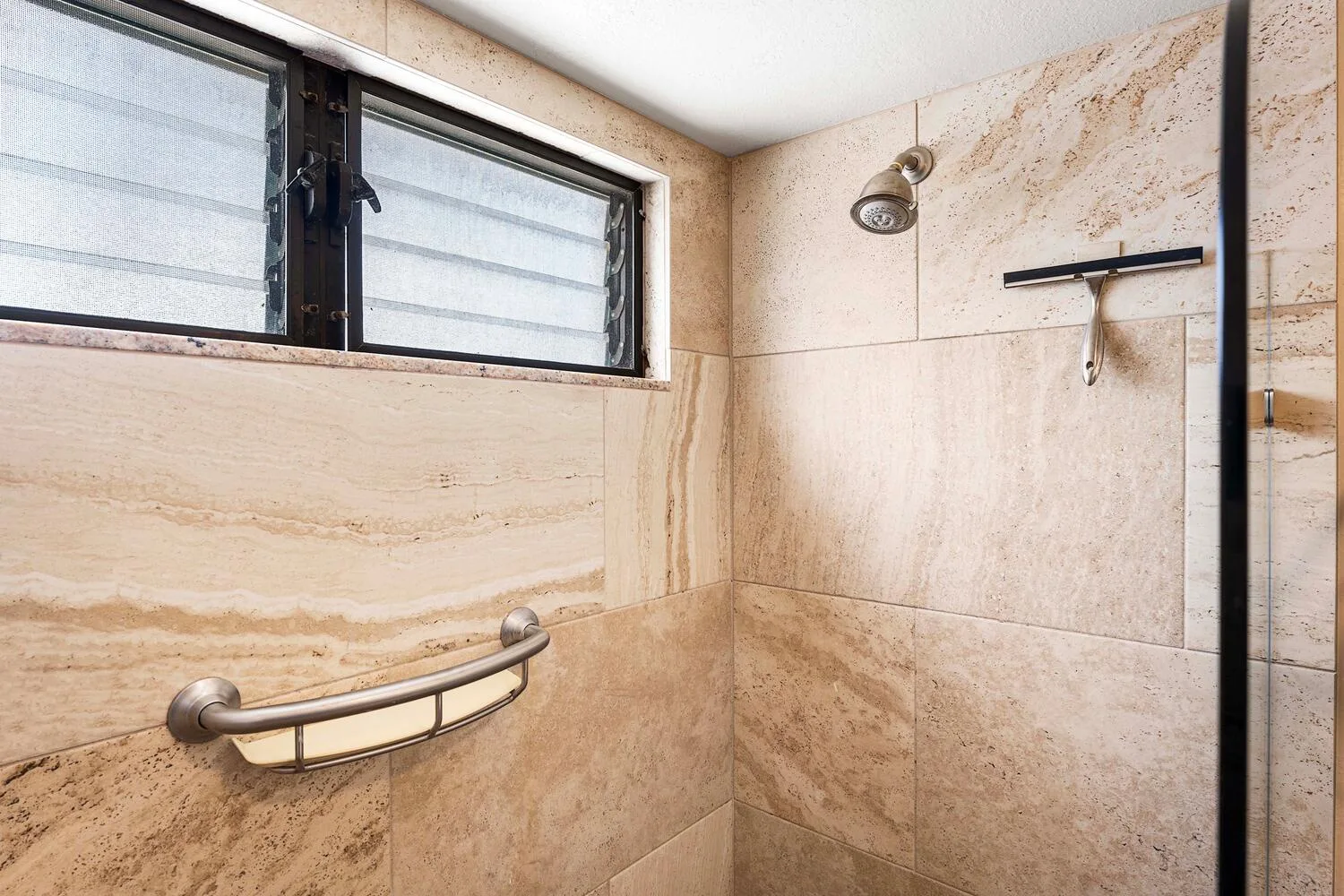 Una zona de ducha con azulejos, una ventana alta y accesorios en la pared.