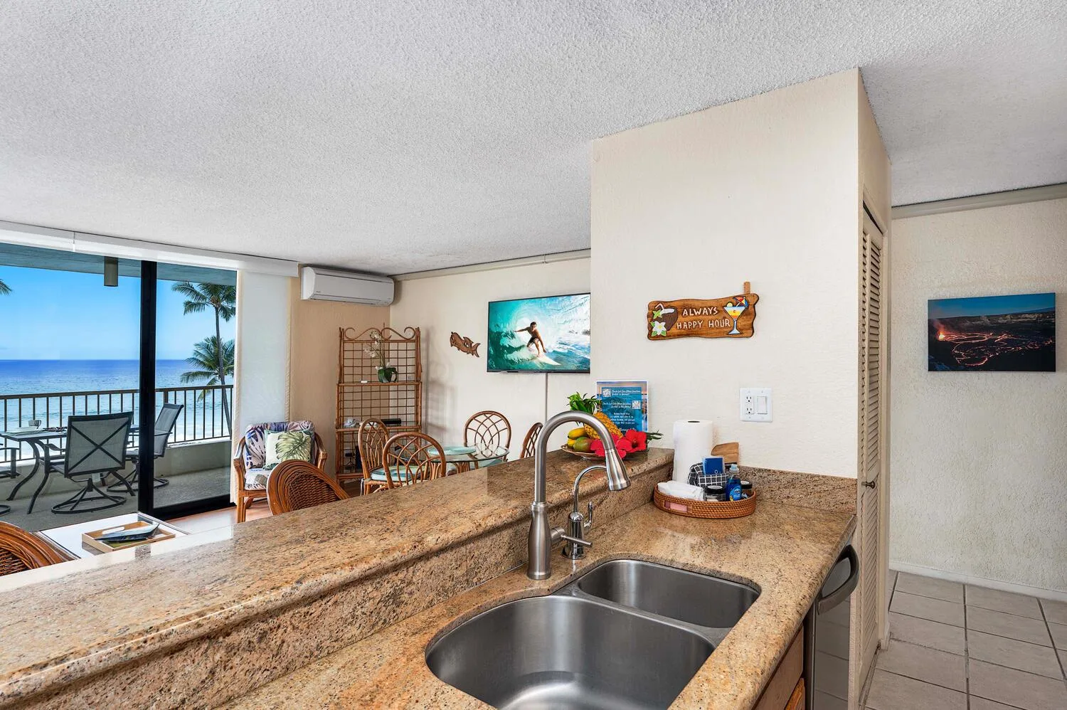 Una encimera de cocina y un fregadero dan a un comedor junto a un balcón con vistas al mar.