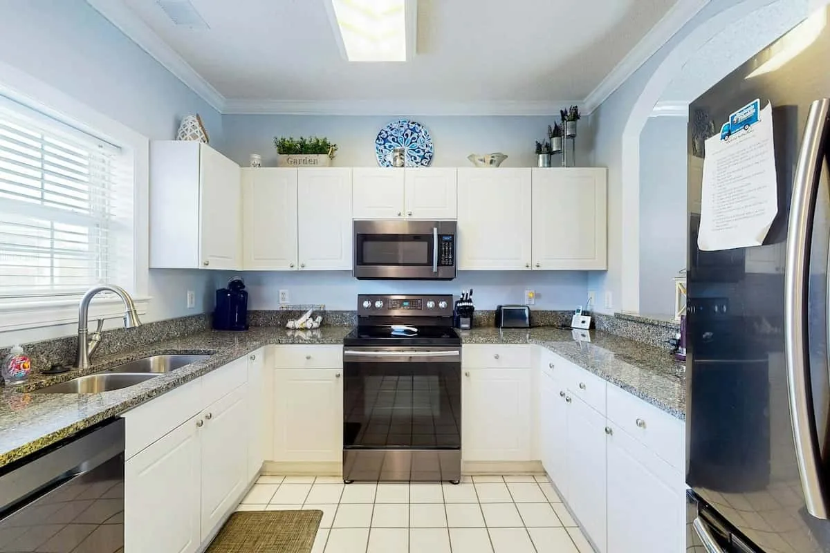 Una cocina luminosa con gabinetes blancos, encimeras de piedra y una estufa central.