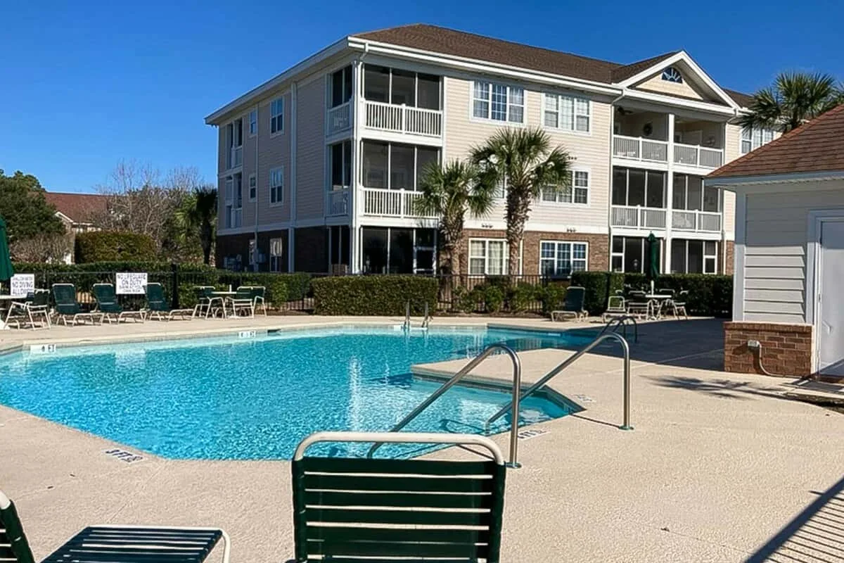 Una piscina al aire libre está junto a un edificio residencial de varios pisos en un día soleado.