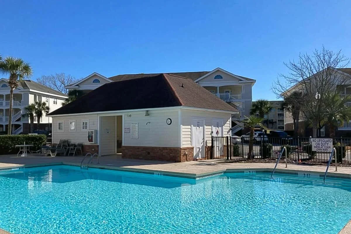 Una piscina al aire libre junto a un edificio pequeño y edificios de apartamentos alrededor.