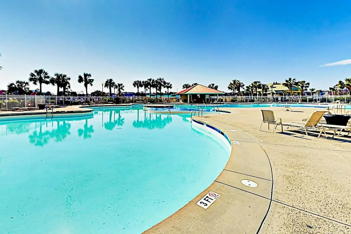 Una piscina al aire libre se curva junto a una terraza soleada con asientos.
