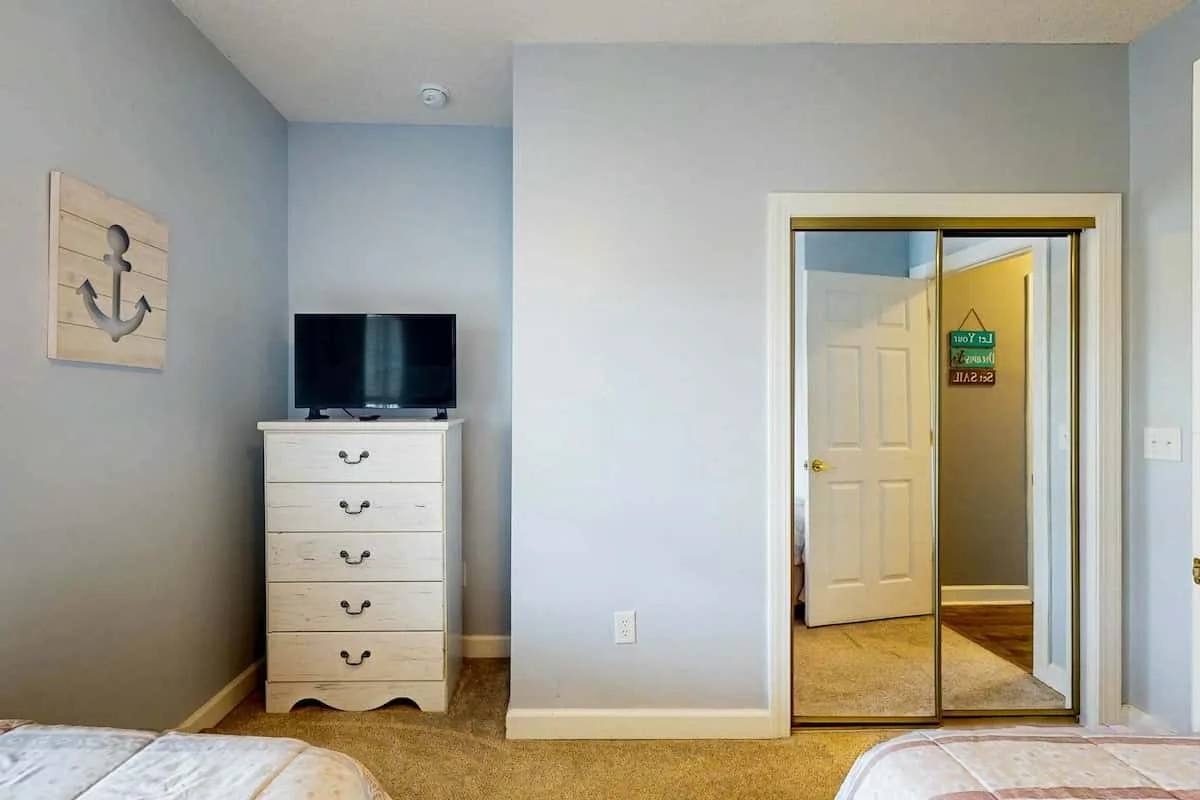Un dormitorio con un televisor sobre una cómoda y una puerta de armario con espejo.