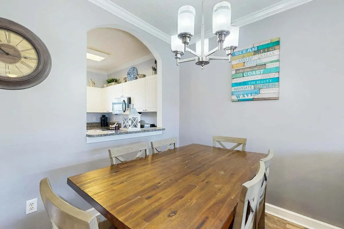 Comedor con una mesa de madera, asientos y una cocina visible a través de un arco.